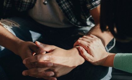 Close up of man's clenched hands with a woman's hand resting on his arm. Adobe